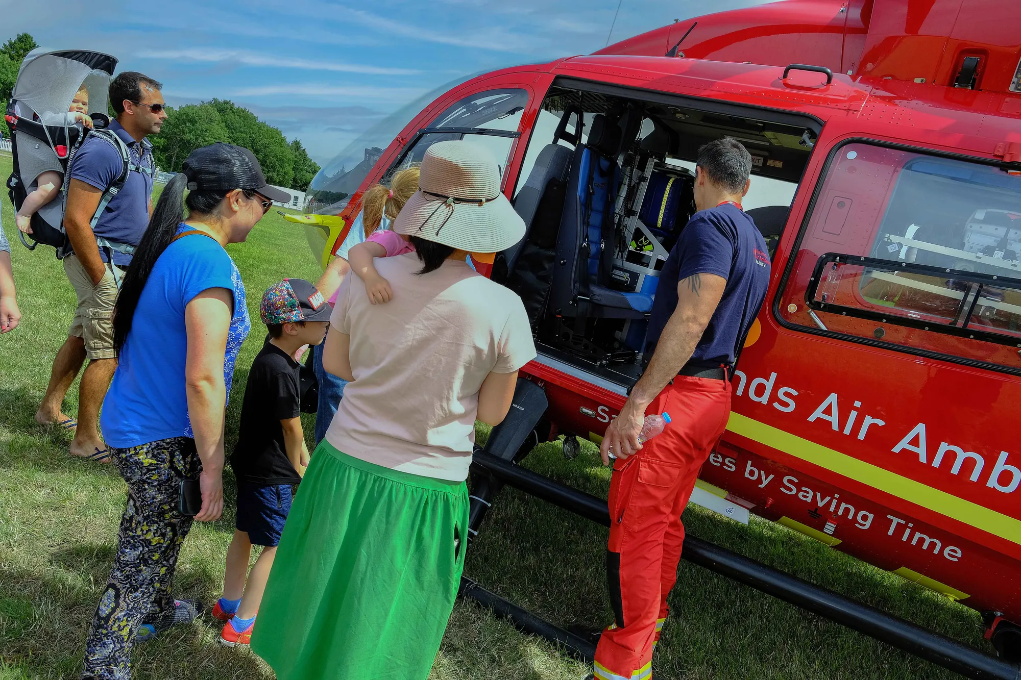 Maac People Standing Around A Red Helicopter With A Man In A Hat