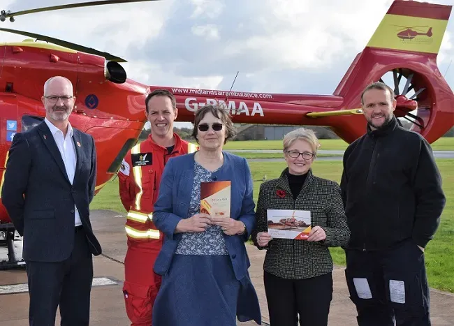 Maac People Standing In Front Of A Helicopter With A Man Holding A Book
