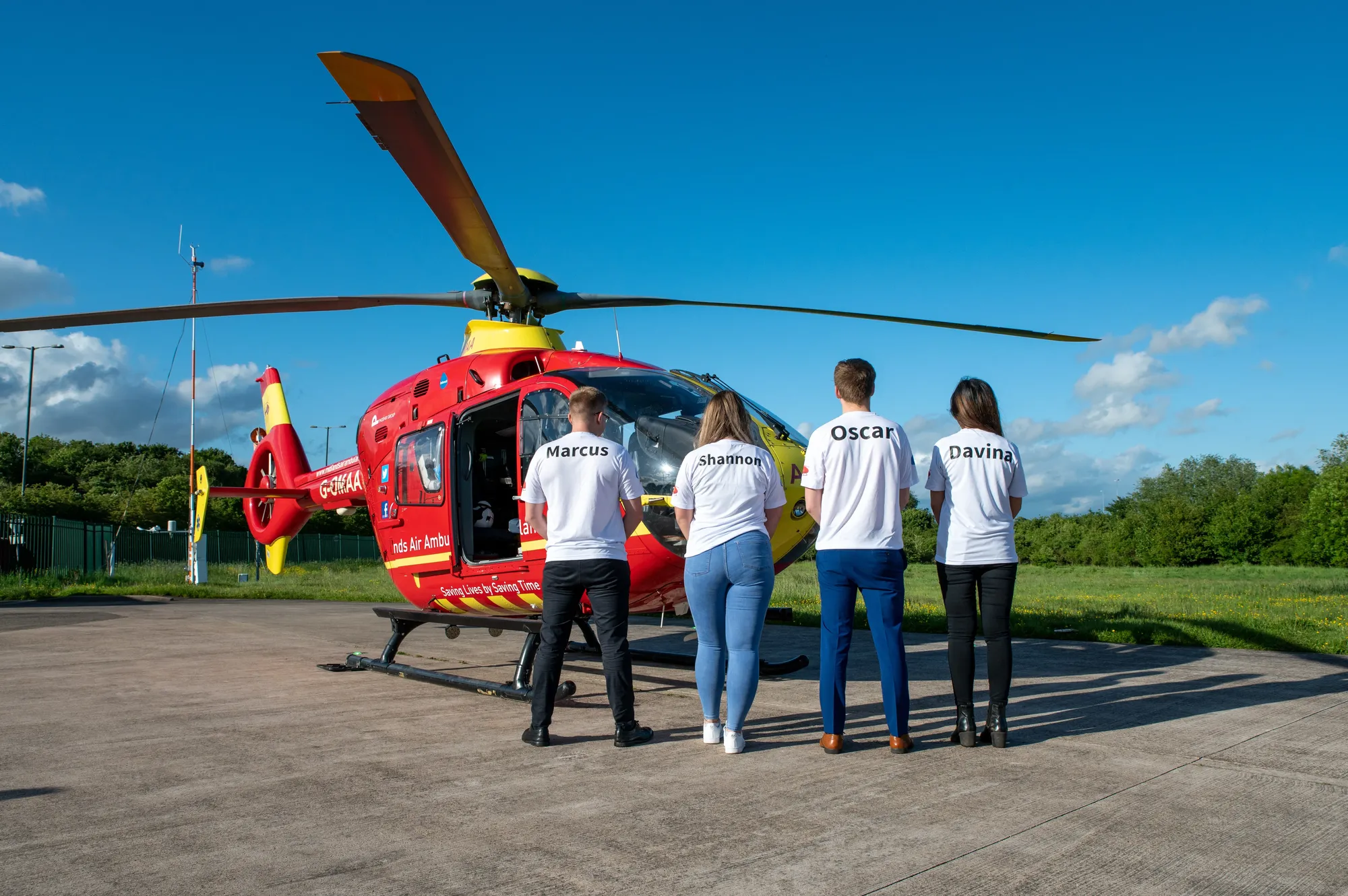 Maac People Standing In Front Of A Helicopter With A Man Standing Next To It