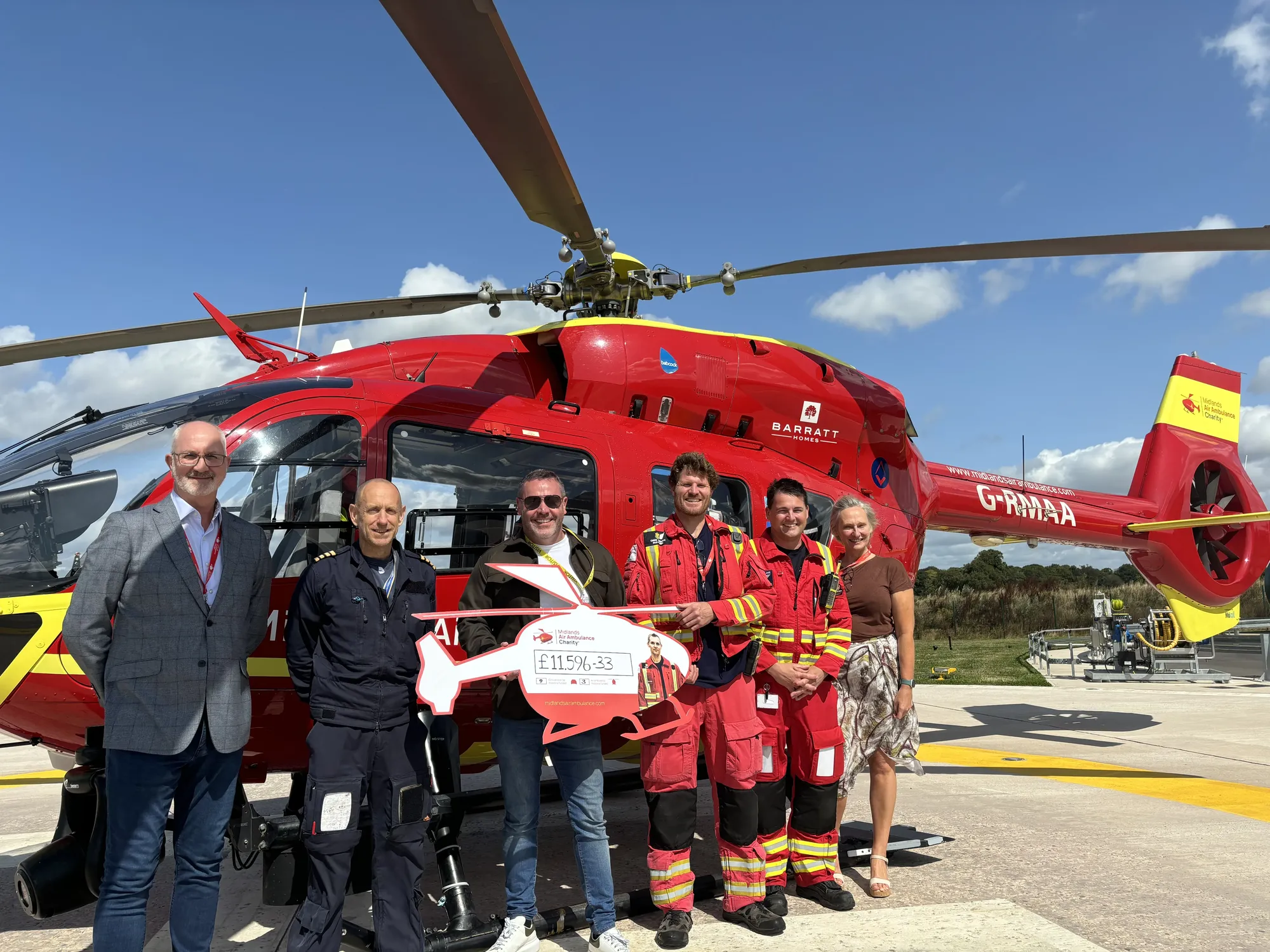 Maac People Standing In Front Of A Helicopter With A Ribbon In Front Of It