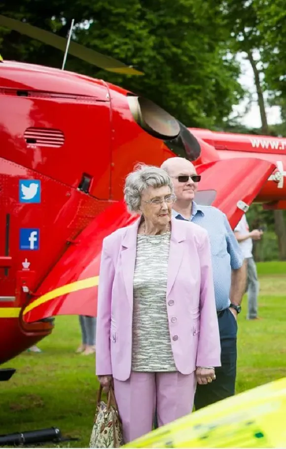Maac People Standing In Front Of A Helicopter With A Woman In A Pink Suit
