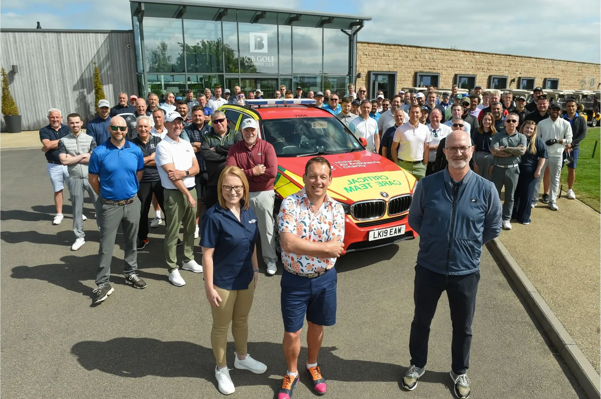 Maac People Standing In Front Of A Red And Yellow Car With A Group Of People Standing Around It