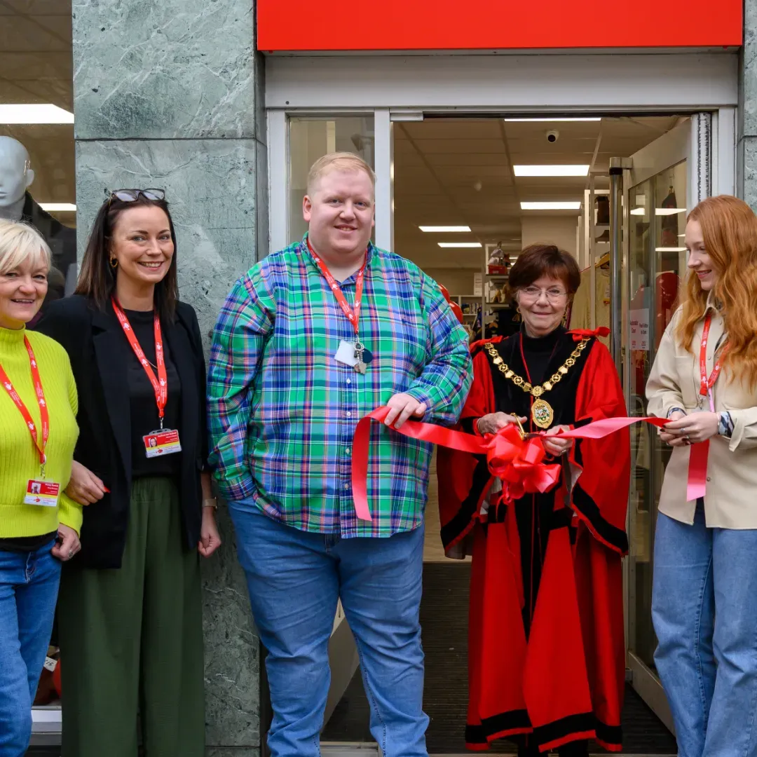 Maac People Standing Outside Of A Store Holding A Ribbon And Scissors