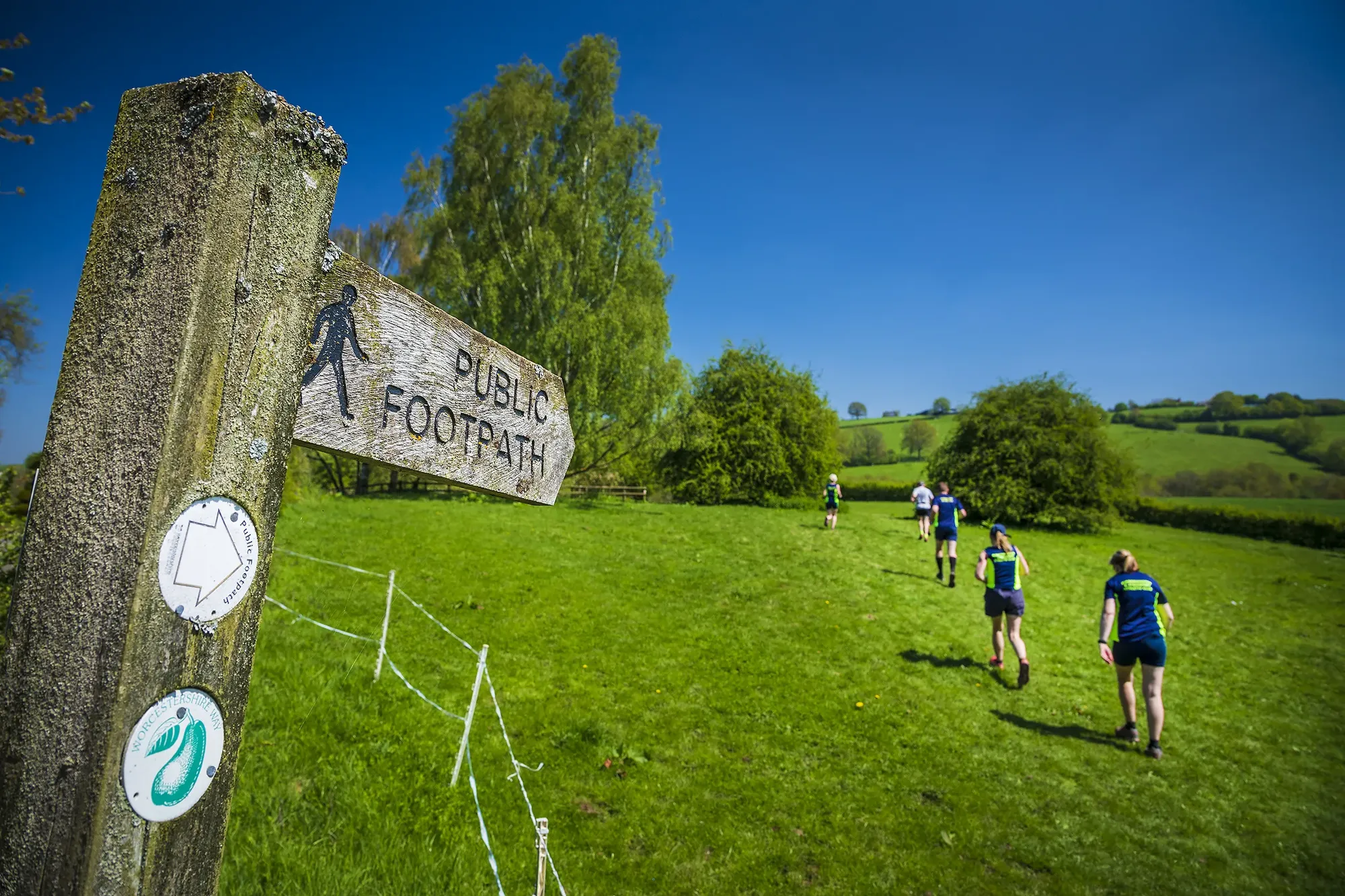 Maac Several People Walking On A Path In A Field With A Sign
