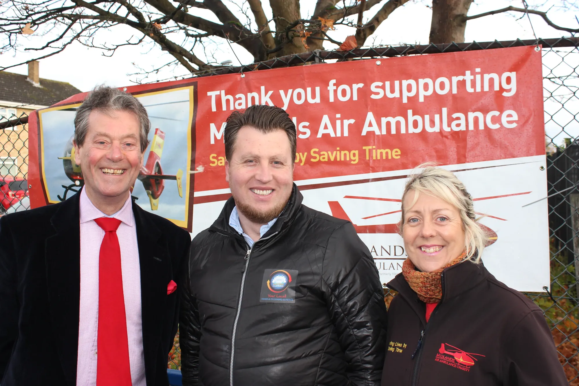 Maac Smiling Man And Woman Standing Next To A Banner With A Man In A Red Tie