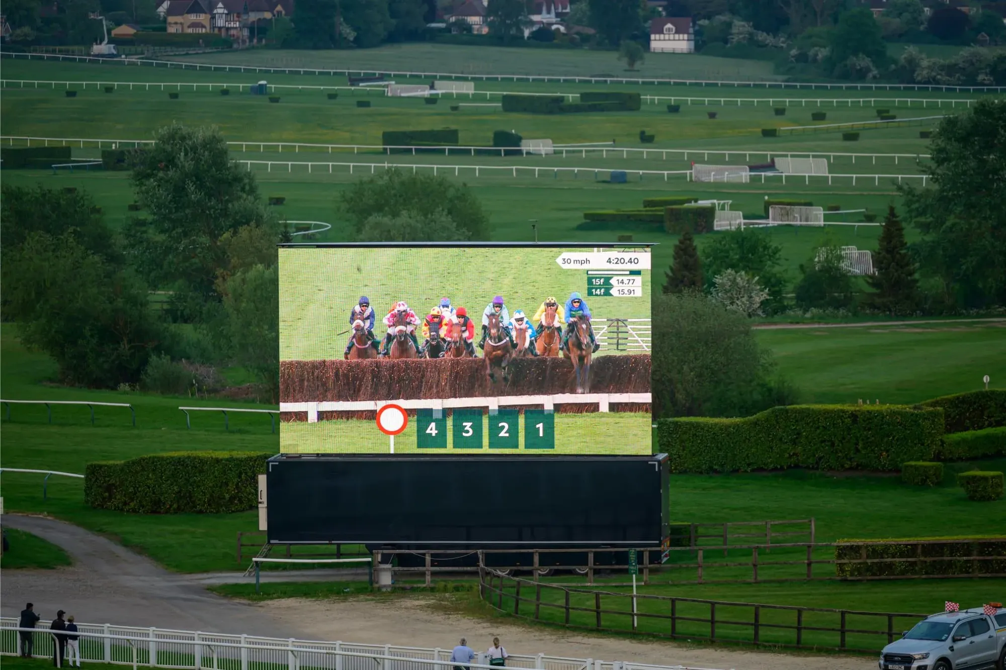 Maac There Is A Large Screen Showing A Horse Race On The Field