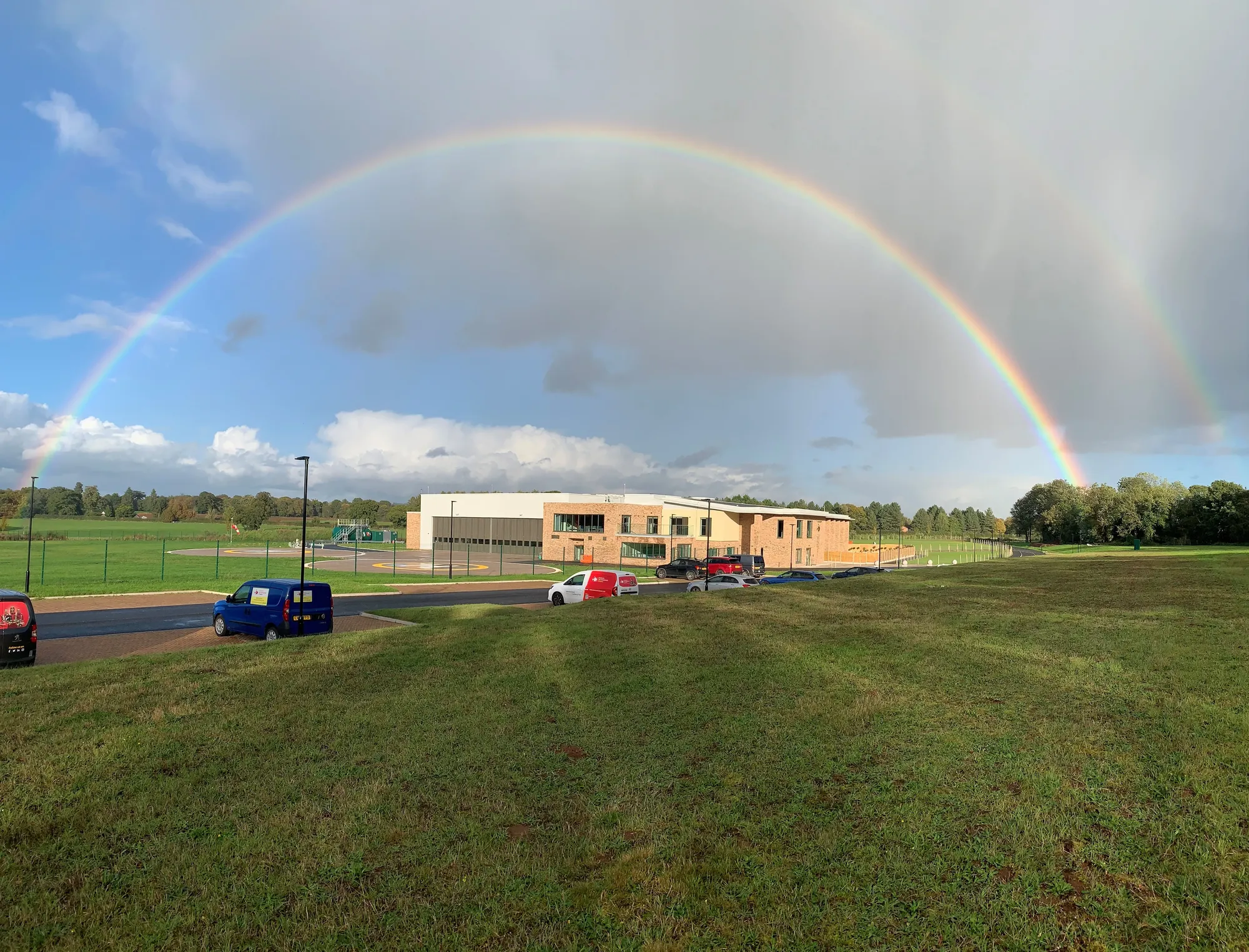 Maac There Is A Rainbow In The Sky Over A School With Cars Parked In The Grass