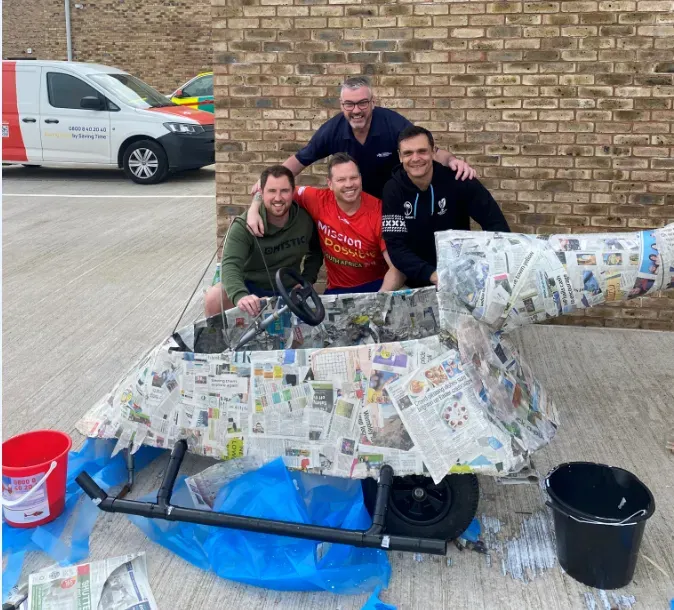 Maac Three Men Are Posing With A Large Piece Of Newspaper On A Cart