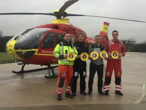 Maac Three Men In Red And Yellow Uniforms Standing In Front Of A Helicopter