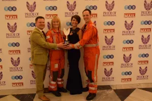 Maac Three People In Orange Suits Holding A Trophy In Front Of A Wall