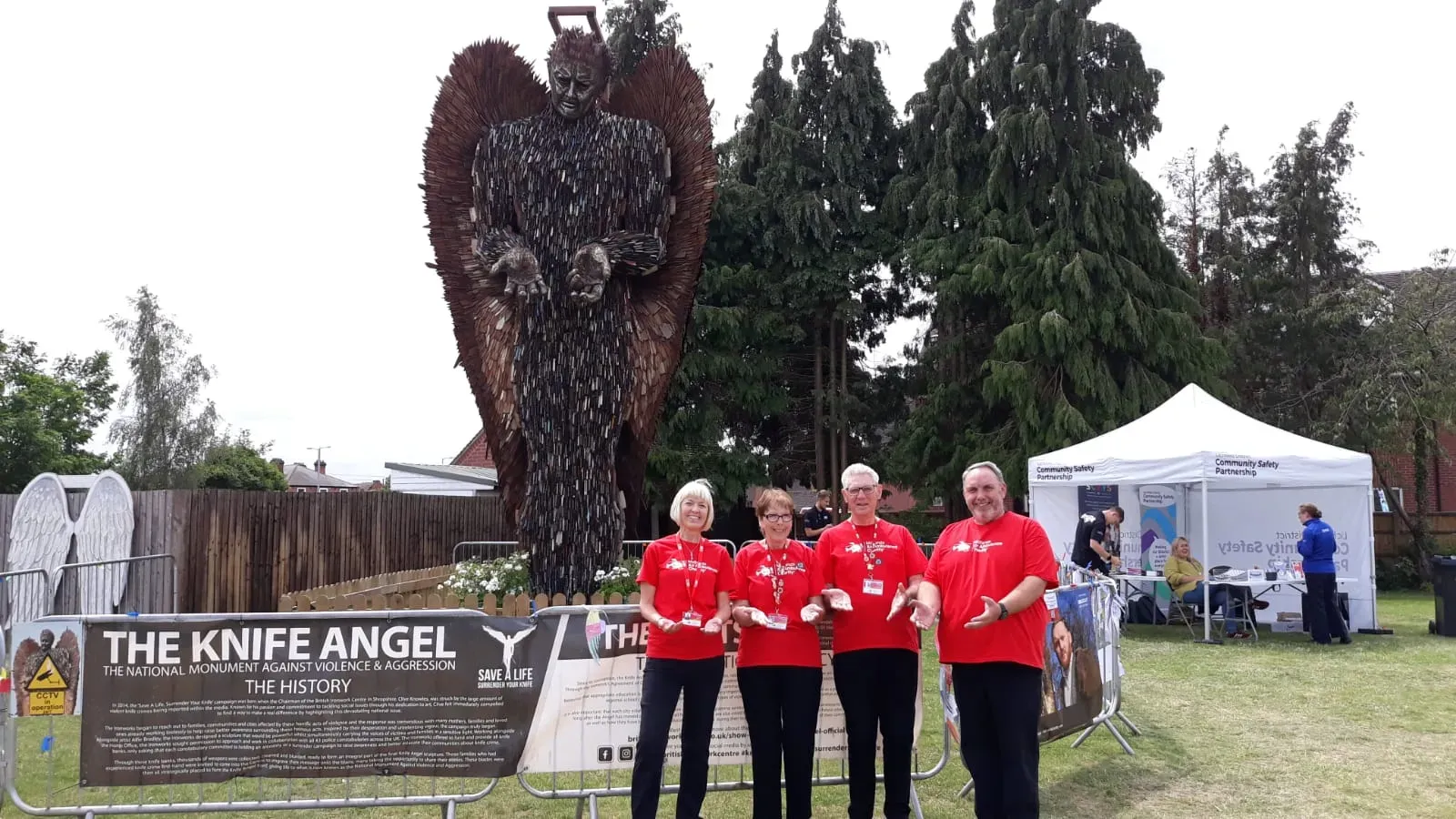 Maac Three People In Red Shirts Standing In Front Of A Statue Of An Angel