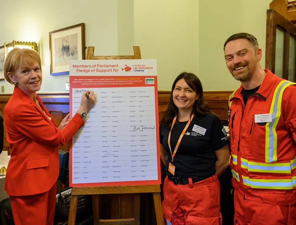 Maac Three People In Red Work Clothes Standing Next To A Sign
