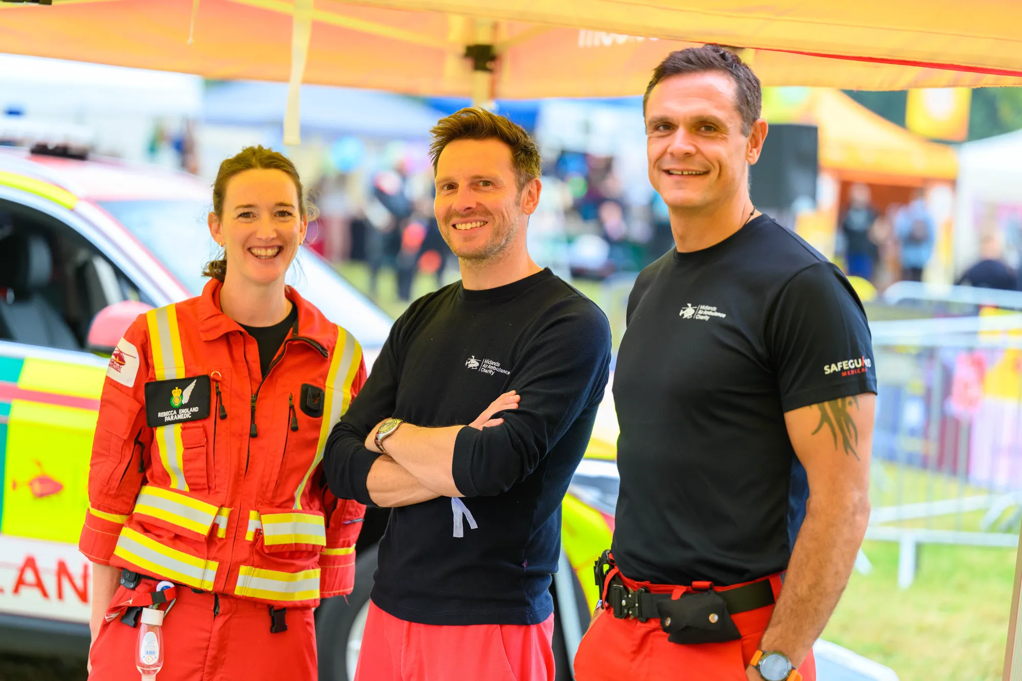 Maac Three People Standing Under A Tent With A Car In The Background