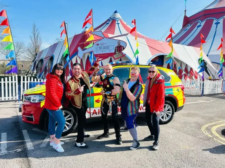 Maac Three Women Standing In Front Of A Car With A Circus Tent In The Background