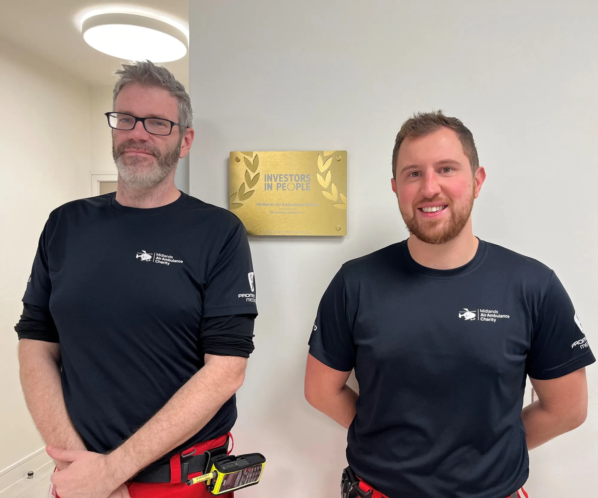 Maac Two Men In Black Shirts Standing Next To Each Other Holding Tools