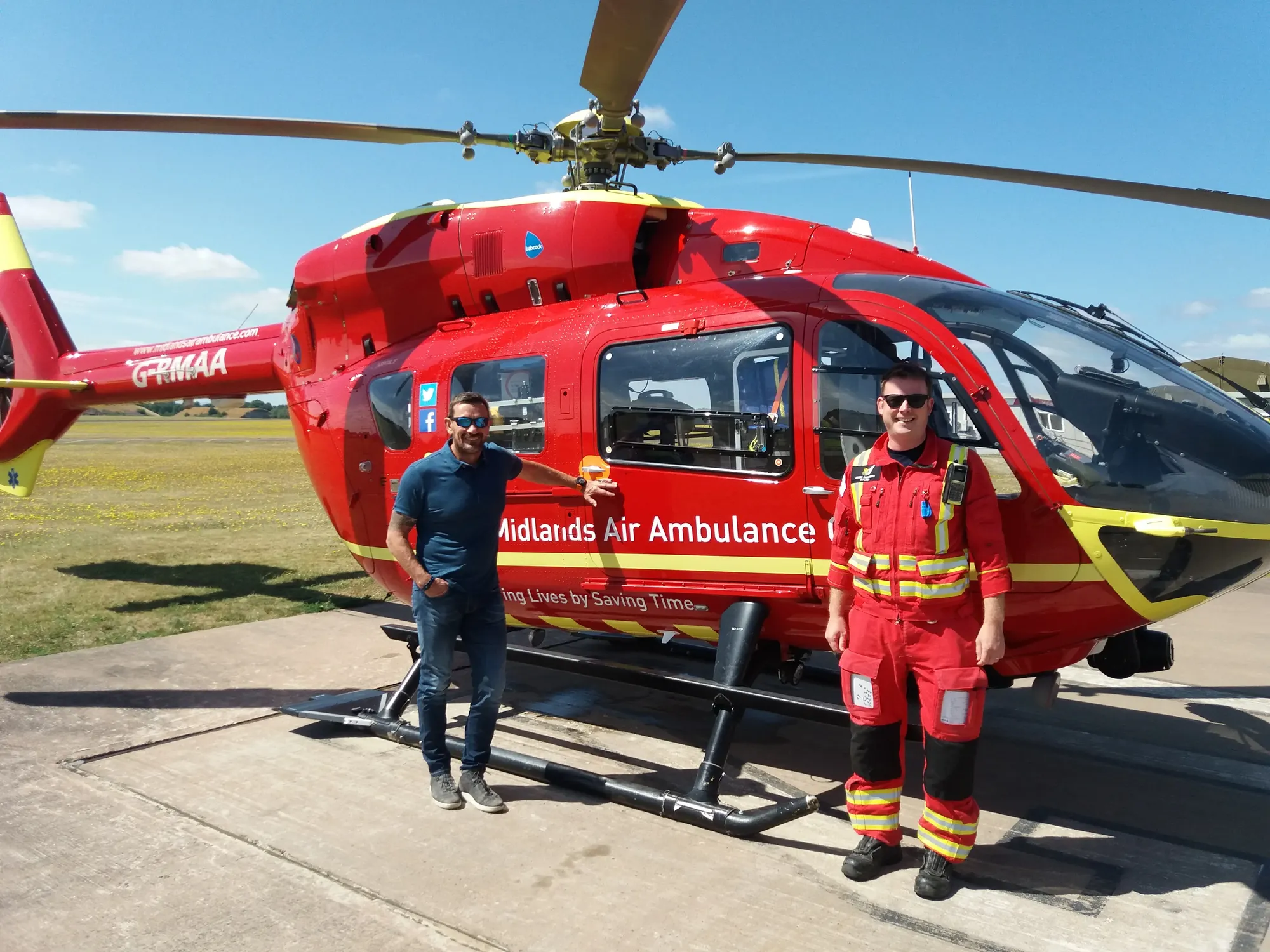 Maac Two Men Standing Next To A Helicopter On A Runway