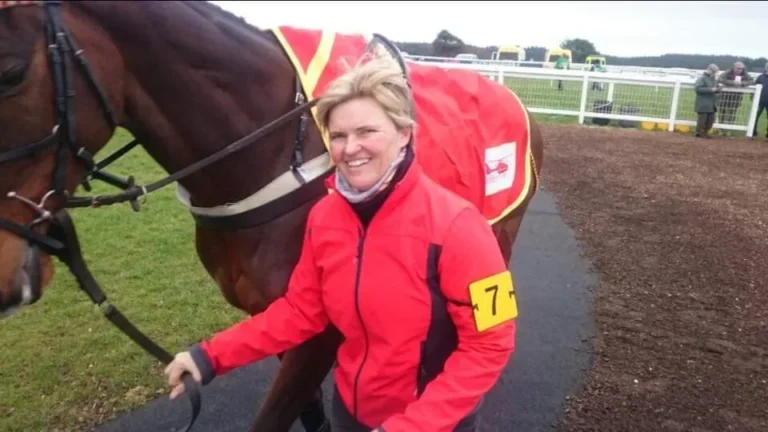 Maac Woman In Red Jacket Standing Next To A Horse With A Number On It