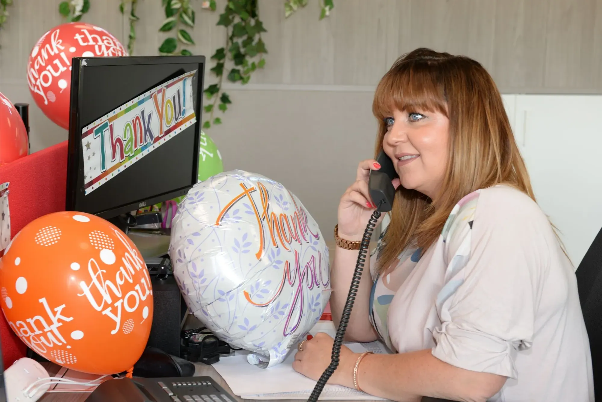 Maac Woman Sitting At Desk With Balloons And Phone In Front Of Her